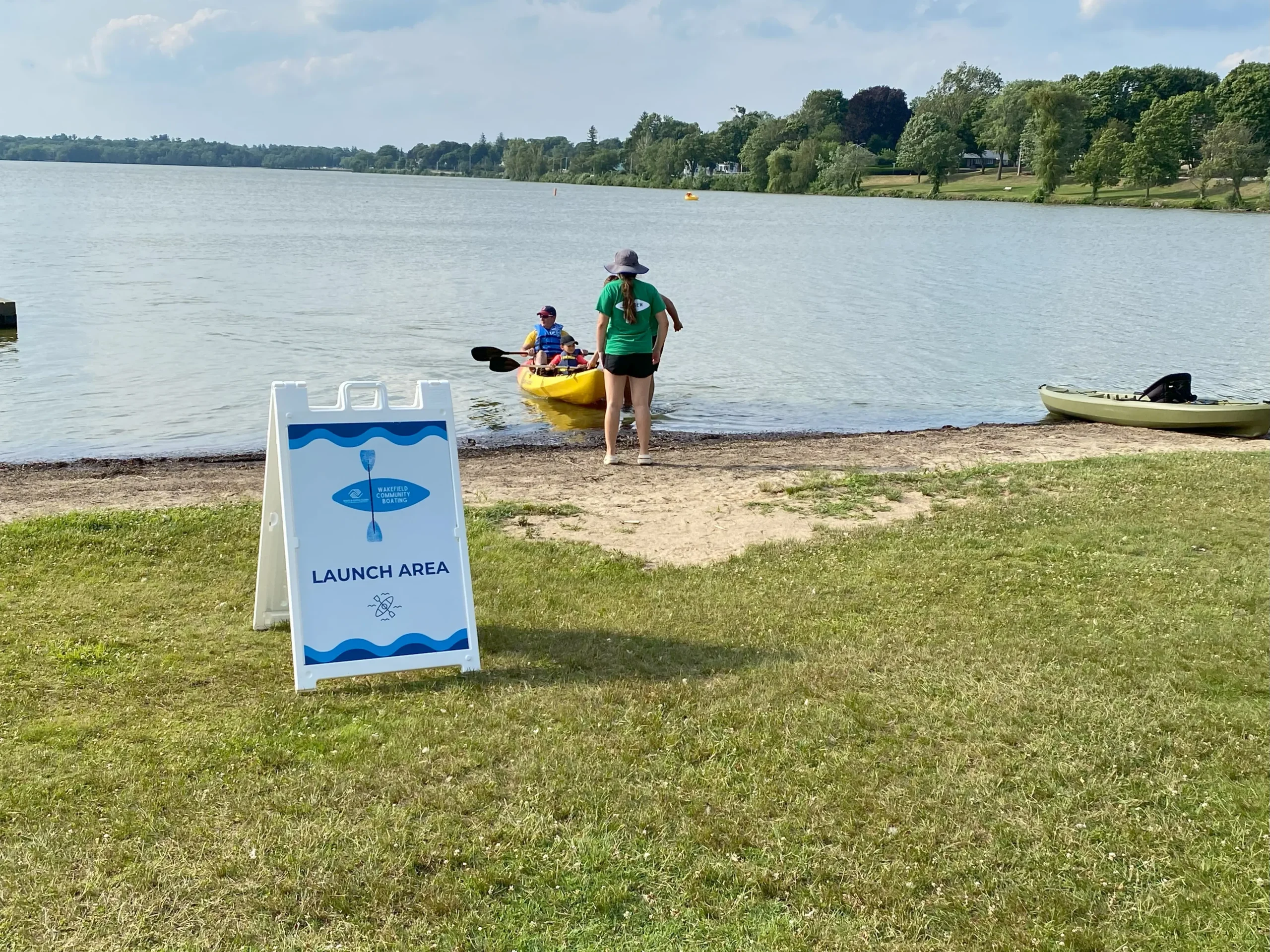 A BGC staff member assists a family launching a tandem kayak at Lake Quannapowitt